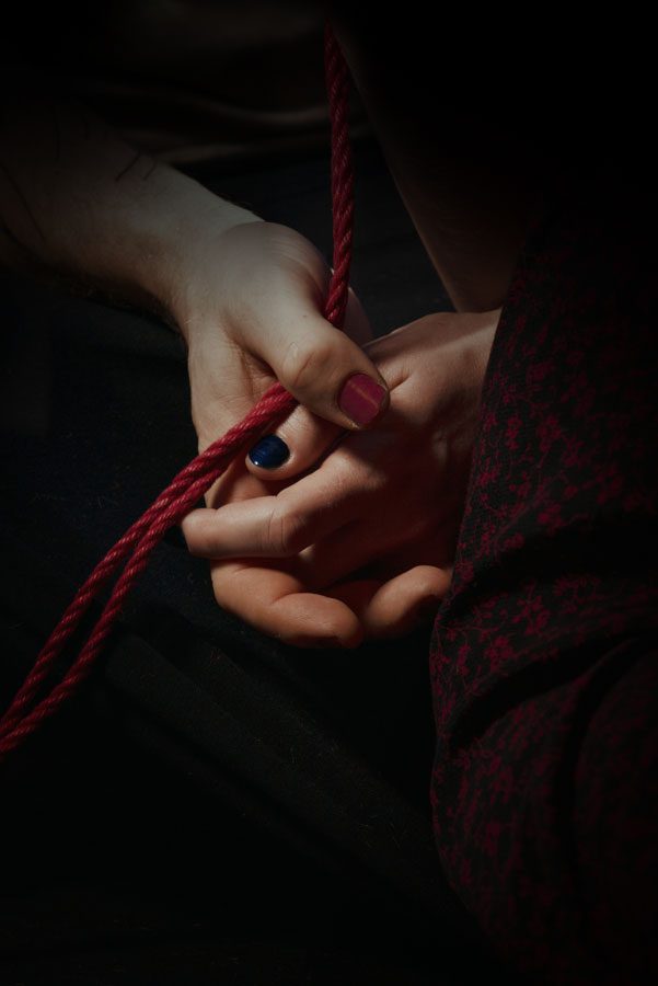 A photo of two people's hands clasped around a red rope.